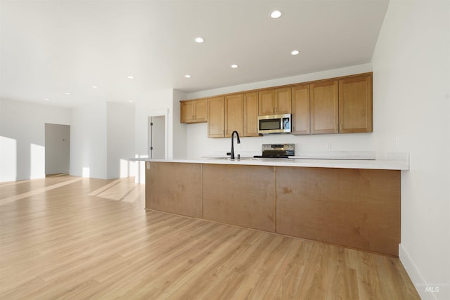 kitchen with sink, light hardwood / wood-style floors, kitchen peninsula, and appliances with stainless steel finishes