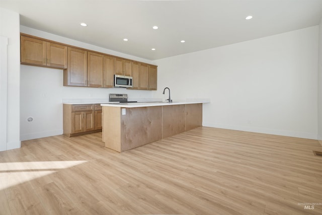 kitchen featuring appliances with stainless steel finishes, sink, a breakfast bar area, kitchen peninsula, and light wood-type flooring