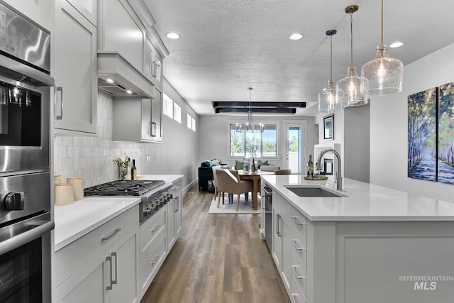 kitchen featuring sink, stainless steel appliances, tasteful backsplash, an island with sink, and pendant lighting