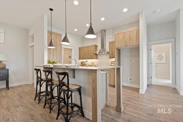 kitchen with pendant lighting, tasteful backsplash, wall chimney range hood, a breakfast bar, and light wood-type flooring