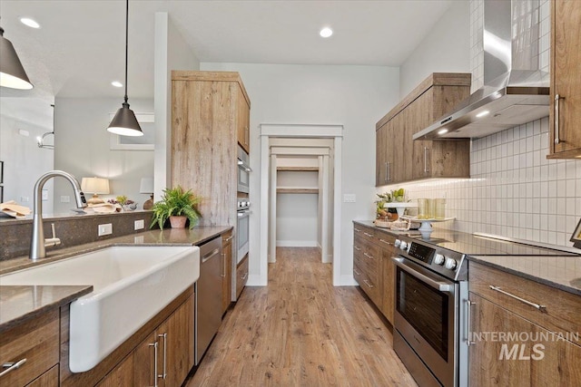 kitchen featuring wall chimney exhaust hood, pendant lighting, stainless steel appliances, light hardwood / wood-style flooring, and sink