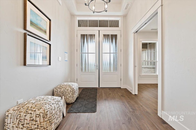 entrance foyer featuring a notable chandelier, wood-type flooring, french doors, and a raised ceiling