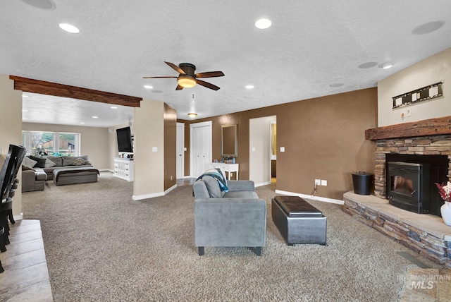 carpeted living room with a textured ceiling, ceiling fan, and a stone fireplace