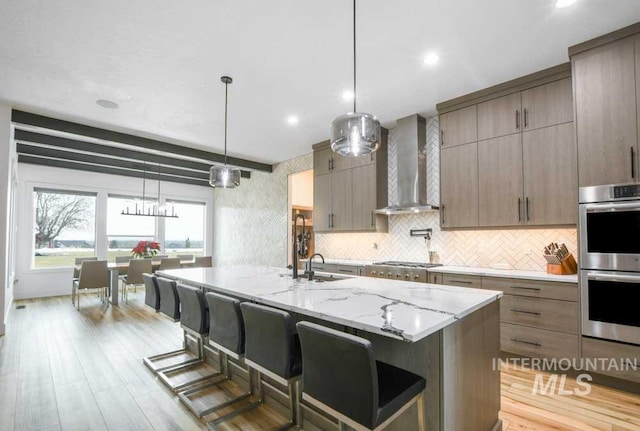 kitchen featuring pendant lighting, a large island, wall chimney exhaust hood, stainless steel appliances, and light wood-type flooring