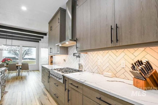 kitchen with tasteful backsplash, stainless steel gas cooktop, light hardwood / wood-style flooring, wall chimney range hood, and light stone countertops