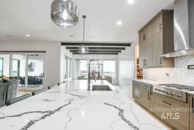 kitchen with pendant lighting, sink, stainless steel gas stovetop, wall chimney range hood, and decorative backsplash