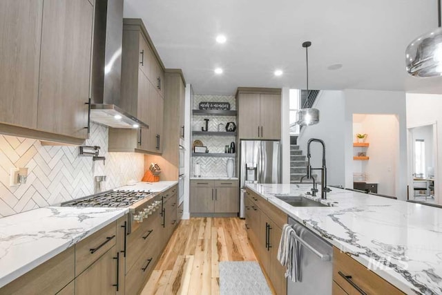 kitchen featuring pendant lighting, light wood-type flooring, sink, wall chimney exhaust hood, and stainless steel appliances