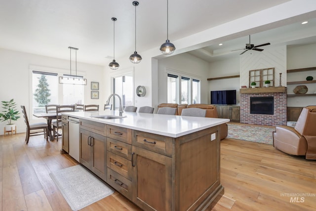 kitchen with a sink, dishwasher, light wood-style flooring, hanging light fixtures, and a kitchen island with sink