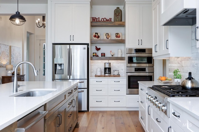 kitchen with a sink, open shelves, ventilation hood, appliances with stainless steel finishes, and light countertops