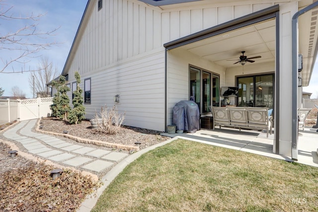 exterior space featuring board and batten siding, ceiling fan, fence, a lawn, and a patio area