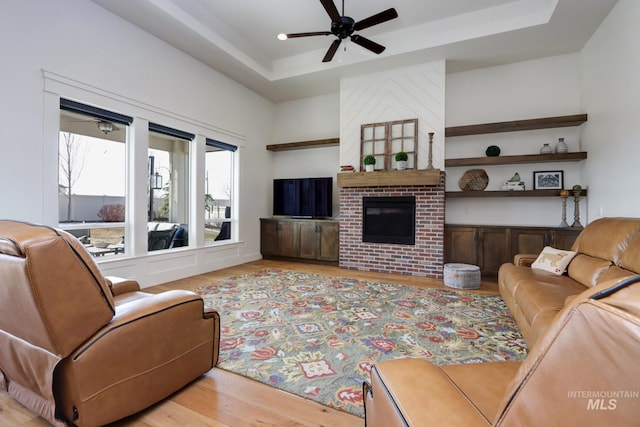 living room featuring a fireplace, a tray ceiling, light wood-style floors, and ceiling fan