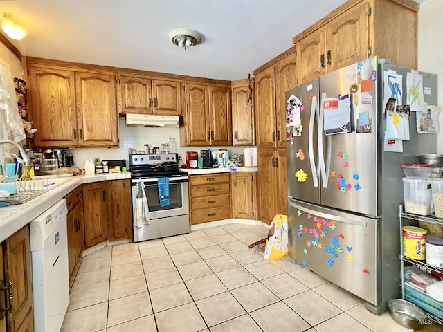 kitchen featuring stainless steel appliances, brown cabinets, under cabinet range hood, and light tile patterned flooring