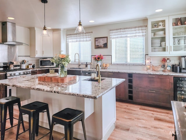 kitchen with sink, wall chimney exhaust hood, hanging light fixtures, backsplash, and light wood-type flooring