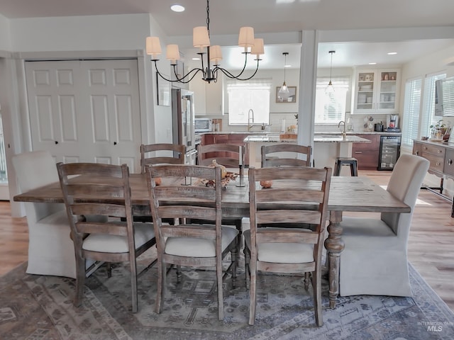 dining space with a notable chandelier, plenty of natural light, wood-type flooring, and beverage cooler