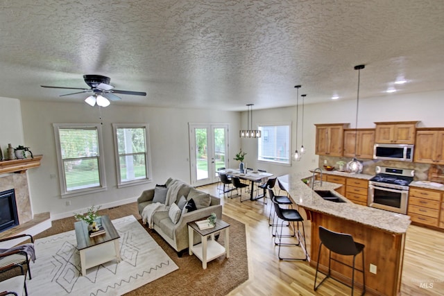 living room with french doors, sink, ceiling fan, light wood-type flooring, and a textured ceiling