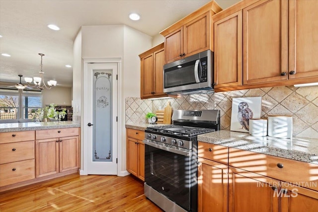 kitchen featuring light wood-style floors, appliances with stainless steel finishes, decorative backsplash, a chandelier, and hanging light fixtures