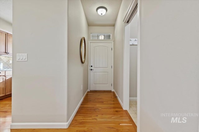 hall with baseboards, a textured ceiling, and light wood-style flooring