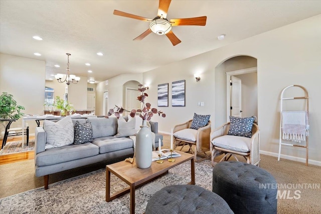 living area featuring baseboards, light colored carpet, ceiling fan with notable chandelier, recessed lighting, and arched walkways