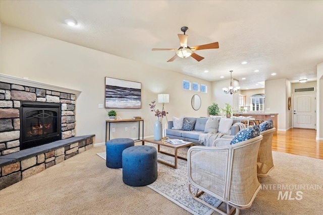 carpeted living area with recessed lighting, baseboards, a stone fireplace, and ceiling fan with notable chandelier