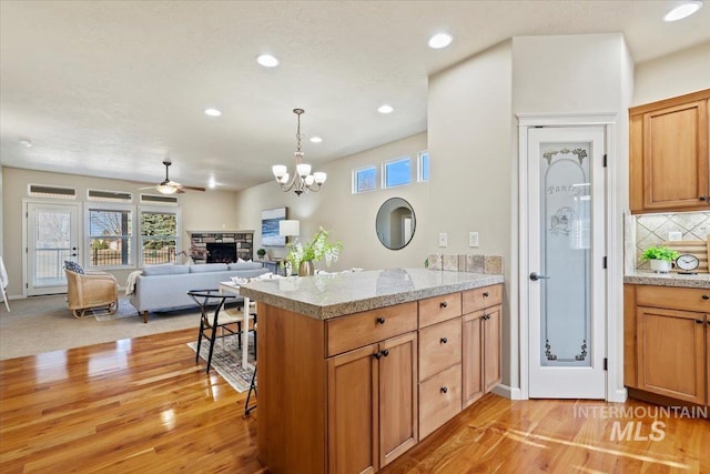 kitchen with light wood finished floors, a stone fireplace, a peninsula, and decorative backsplash