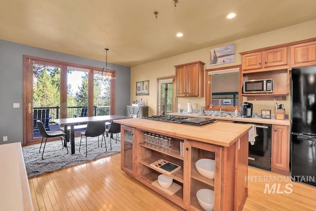 kitchen featuring butcher block countertops, black appliances, decorative light fixtures, and light hardwood / wood-style floors