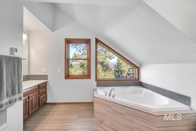 bathroom featuring tiled tub, vanity, and vaulted ceiling