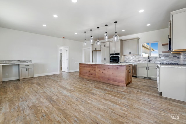 kitchen with appliances with stainless steel finishes, a kitchen island, light wood-style floors, and tasteful backsplash