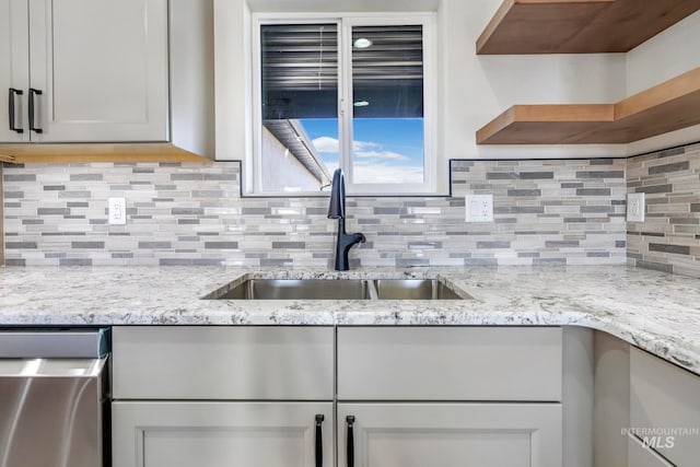 kitchen featuring light stone counters, a sink, dishwasher, open shelves, and tasteful backsplash