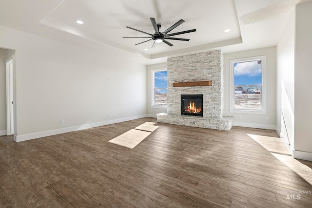 unfurnished living room featuring a tray ceiling, baseboards, and wood finished floors