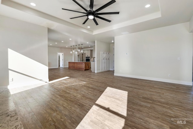 unfurnished living room featuring a ceiling fan, a tray ceiling, wood finished floors, and recessed lighting