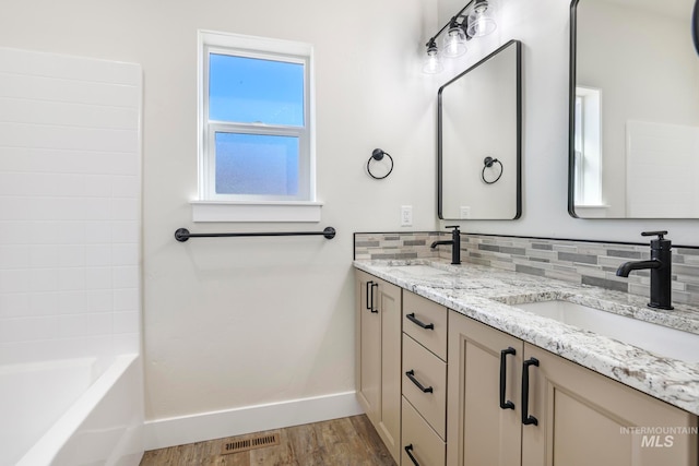 bathroom featuring baseboards, decorative backsplash, a sink, and wood finished floors