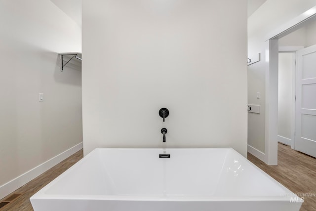 full bath with baseboards, a freestanding bath, and wood finished floors