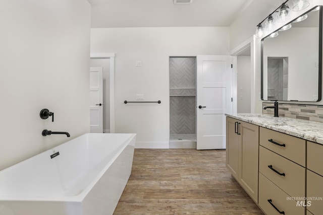 full bath with visible vents, a freestanding bath, decorative backsplash, vanity, and wood finished floors