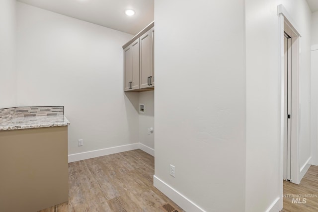 laundry room with baseboards, hookup for a washing machine, cabinet space, and light wood-style floors