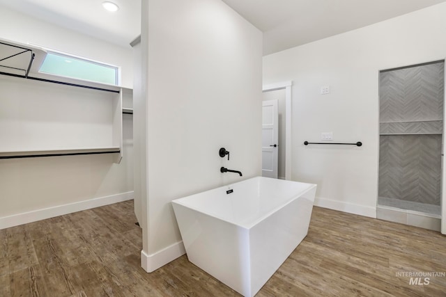 bathroom featuring a freestanding bath, a tile shower, baseboards, and wood finished floors