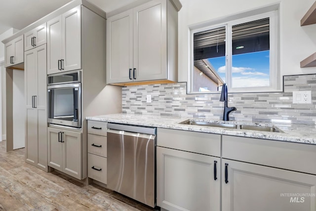 kitchen featuring stainless steel appliances, a sink, light wood-style floors, backsplash, and light stone countertops