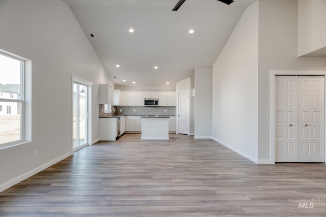 kitchen featuring white cabinets, a sink, stainless steel microwave, open floor plan, and backsplash