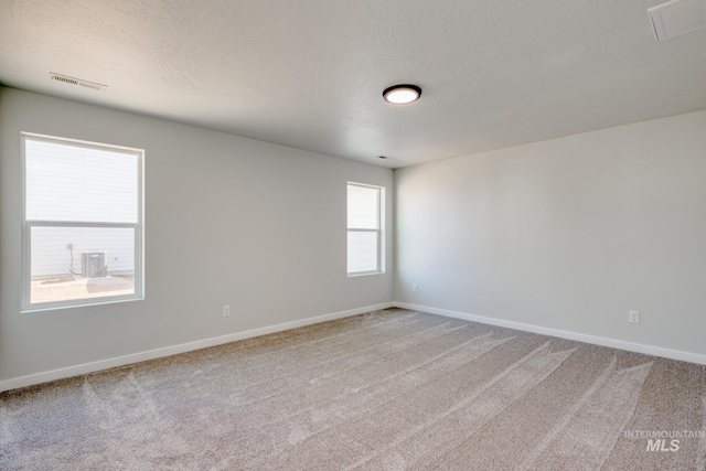 carpeted spare room featuring baseboards, visible vents, and a textured ceiling