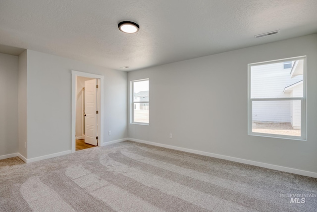 carpeted spare room featuring baseboards, a textured ceiling, and visible vents