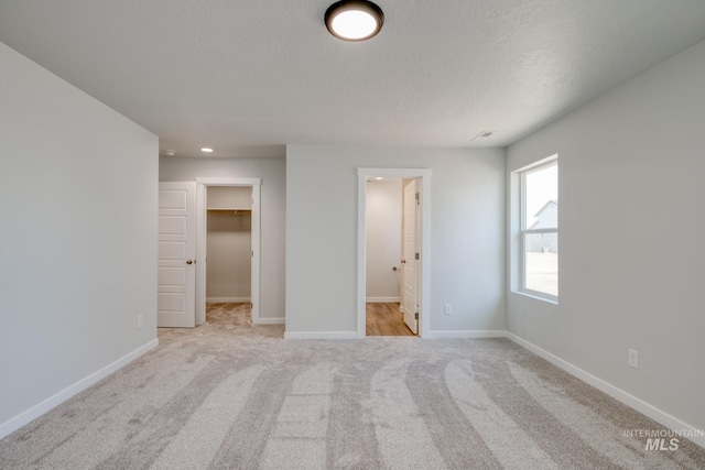 unfurnished bedroom with a walk in closet, baseboards, a textured ceiling, and light colored carpet