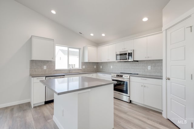 kitchen with lofted ceiling, appliances with stainless steel finishes, a sink, and light wood-style flooring