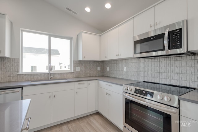 kitchen with stainless steel appliances, a sink, vaulted ceiling, visible vents, and white cabinetry