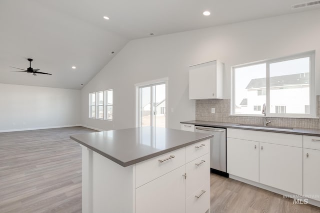kitchen with stainless steel dishwasher, a sink, light wood-type flooring, dark countertops, and backsplash
