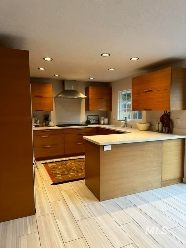 kitchen with wall chimney exhaust hood, stovetop, kitchen peninsula, and sink