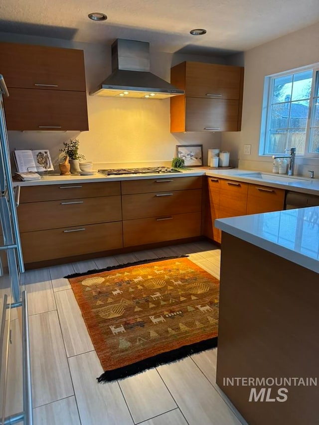 kitchen featuring light wood-type flooring, stainless steel gas cooktop, wall chimney exhaust hood, and sink