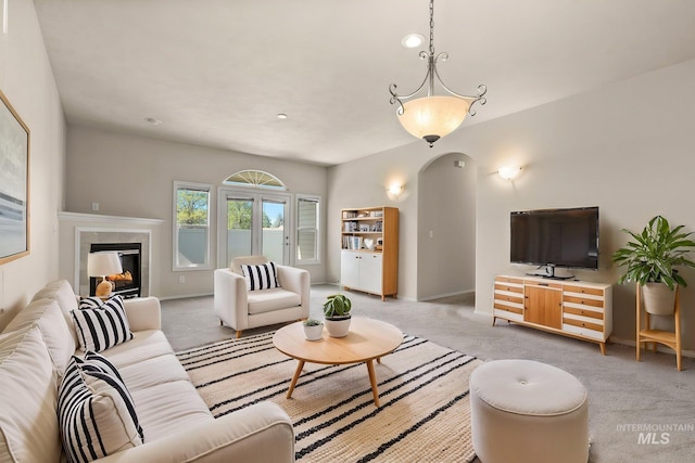 living room with light carpet, a tiled fireplace, and baseboards