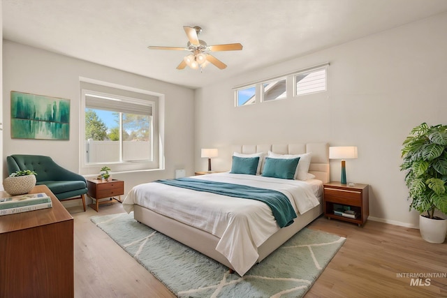bedroom with multiple windows, light wood-type flooring, baseboards, and a ceiling fan
