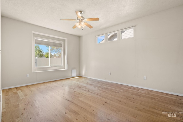 empty room featuring plenty of natural light, ceiling fan, light wood-style floors, baseboards, and a textured ceiling
