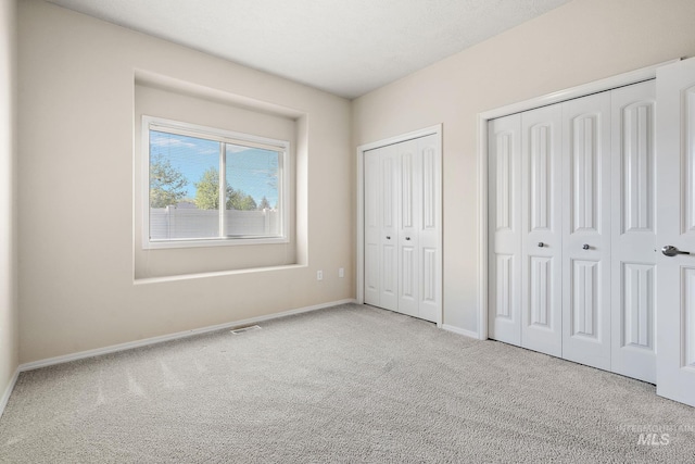 unfurnished bedroom with carpet flooring, two closets, and baseboards