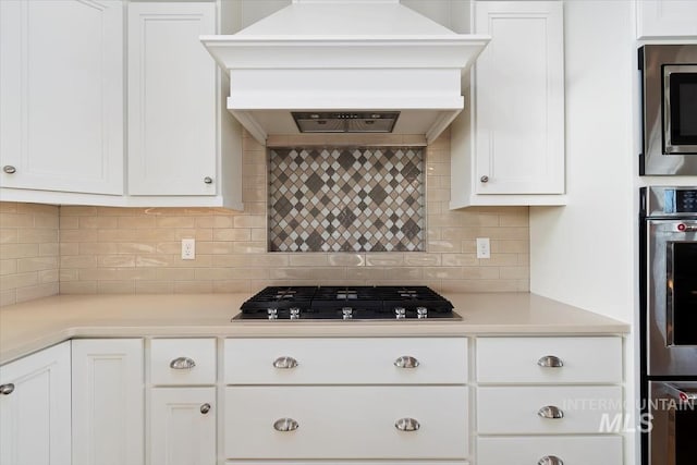 kitchen featuring appliances with stainless steel finishes, white cabinets, light countertops, and custom range hood